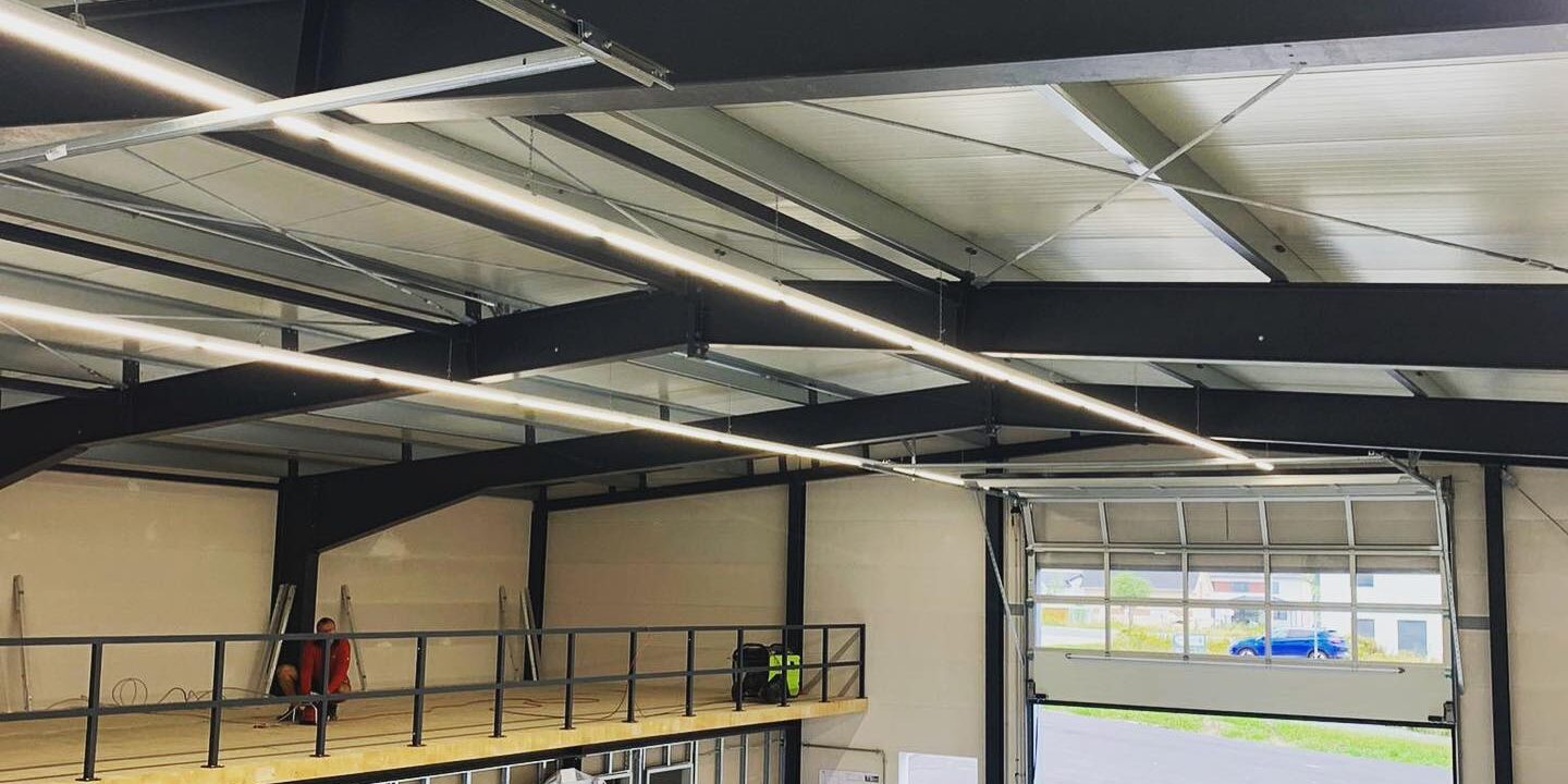 Gewerbehalle mit Stahlkonstruktion, LED-Beleuchtung und installierten Elektrokomponenten während der Bauphase.