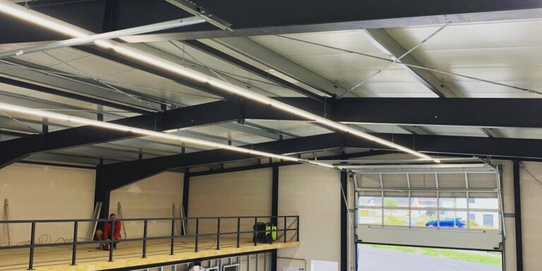 Gewerbehalle mit Stahlkonstruktion, LED-Beleuchtung und installierten Elektrokomponenten während der Bauphase.
