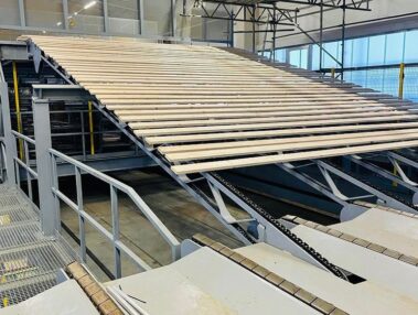 Industrielle Förderanlage transportiert Holzbretter innerhalb einer Produktionshalle der Holzverarbeitung.