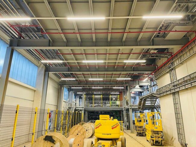 Große Industriehalle mit installierten Kabeltrassen, Beleuchtungssystemen und technischen Anlagen.