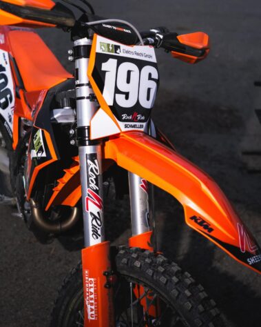 Frontansicht eines orangefarbenen Motocross-Motorrads mit Startnummer und Sponsorenlogo von Elektro Reichl auf der Starttafel.