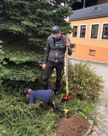 Mitarbeiter und Kind helfen gemeinsam bei der Pflanzung eines Baumes.