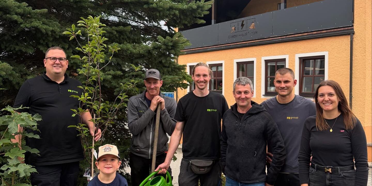 Mitarbeitende und Helfer präsentieren den neu gepflanzten Baum vor dem Firmengebäude.