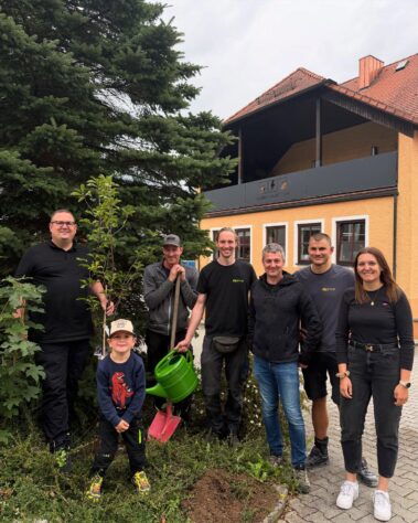 Mitarbeitende und Helfer präsentieren den neu gepflanzten Baum vor dem Firmengebäude.