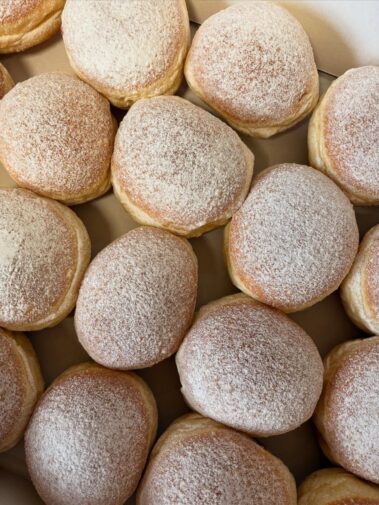 Frisch gebackene Krapfen mit Puderzucker in einer Kiste angeordnet.
