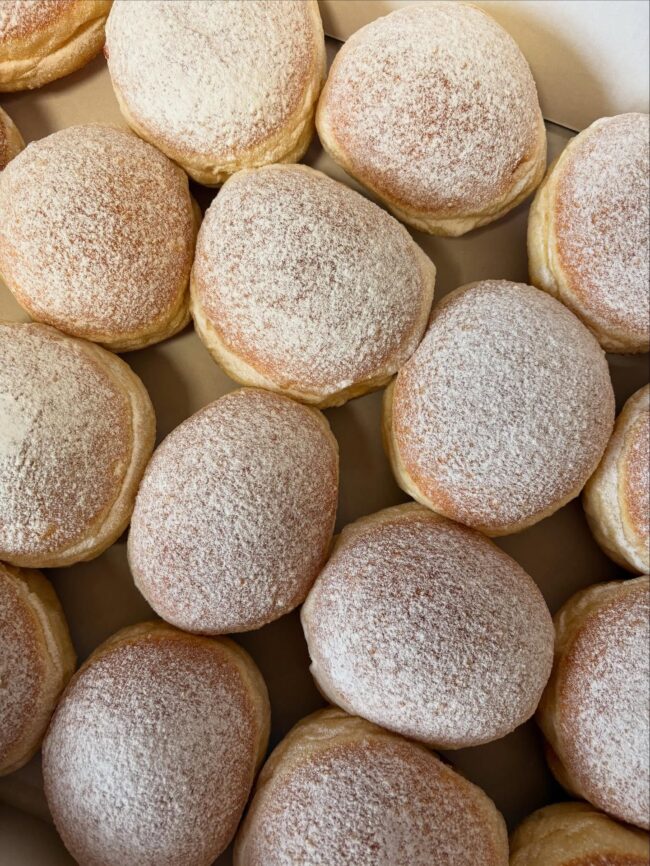 Krapfenaktion für den guten Zweck Frisch gebackene Krapfen mit Puderzucker in einer Kiste angeordnet.