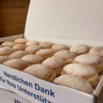 Mehrere mit Puderzucker bestäubte Krapfen in geöffneten Kartons.