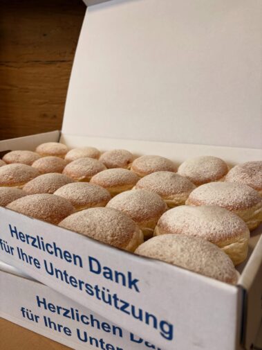 Mehrere mit Puderzucker bestäubte Krapfen in geöffneten Kartons.