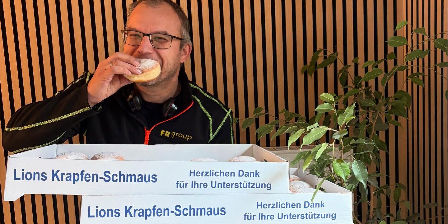 Mitarbeiter hält Krapfenkartons und genießt einen Krapfen während einer Spendenaktion.