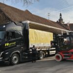 Mitarbeiter und Gabelstapler verladen einen großformatigen Schaltschrank von einem Transportfahrzeug.