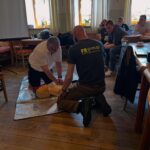 Teilnehmer einer Erste-Hilfe-Schulung verfolgen eine praktische Übung zur Wiederbelebung an einer Übungspuppe.