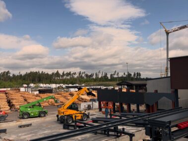Industriegelände mit Holzlager, Maschinen und Fertigungsanlagen für die Verarbeitung von Rundholz und Holzprodukten.
