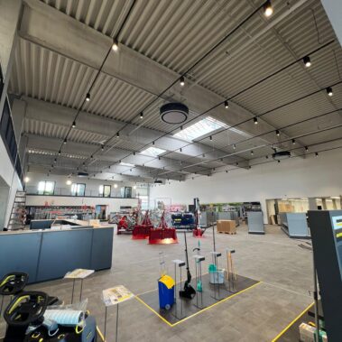 Weitläufige Verkaufs- und Ausstellungsfläche mit Maschinen, Regalsystemen und moderner Beleuchtung in einer Industriehalle mit offener Deckenkonstruktion.