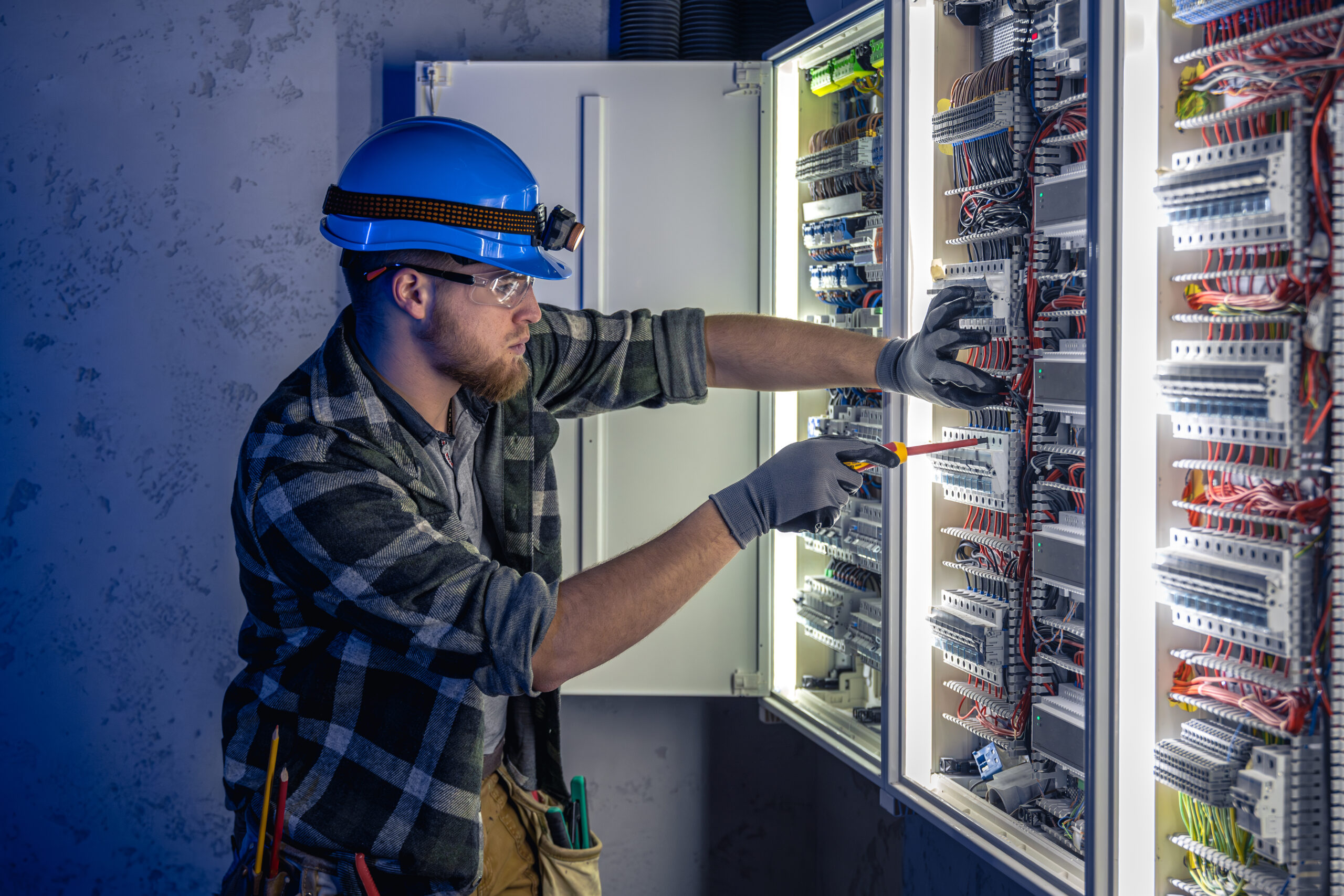 Elektriker arbeitet an einem geöffneten Schaltschrank und prüft die Verdrahtung einer elektrischen Anlage.
