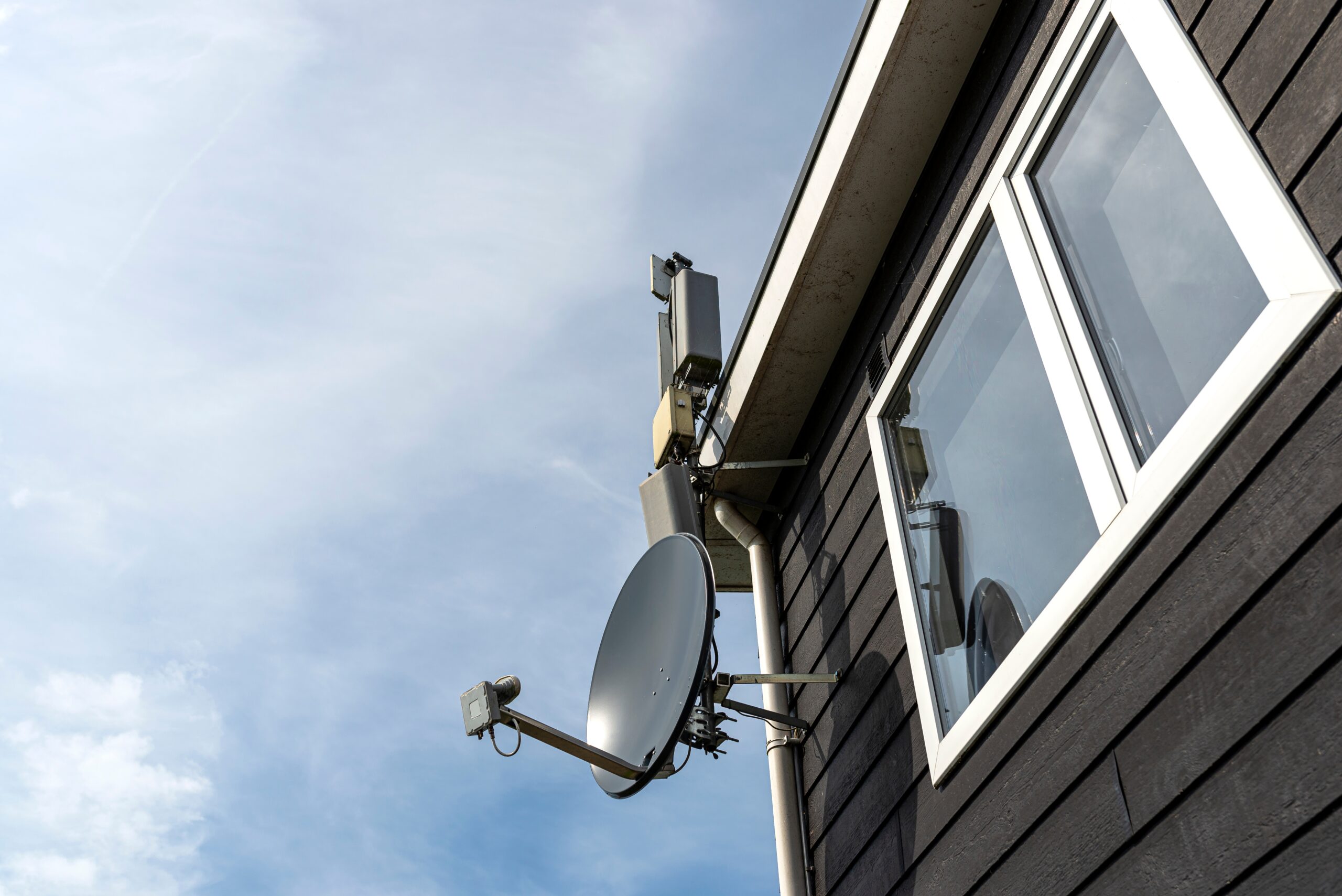 Satellitenschüssel und Kommunikationstechnik an der Außenfassade eines Gebäudes für Empfangs- und Telekommunikationslösungen.