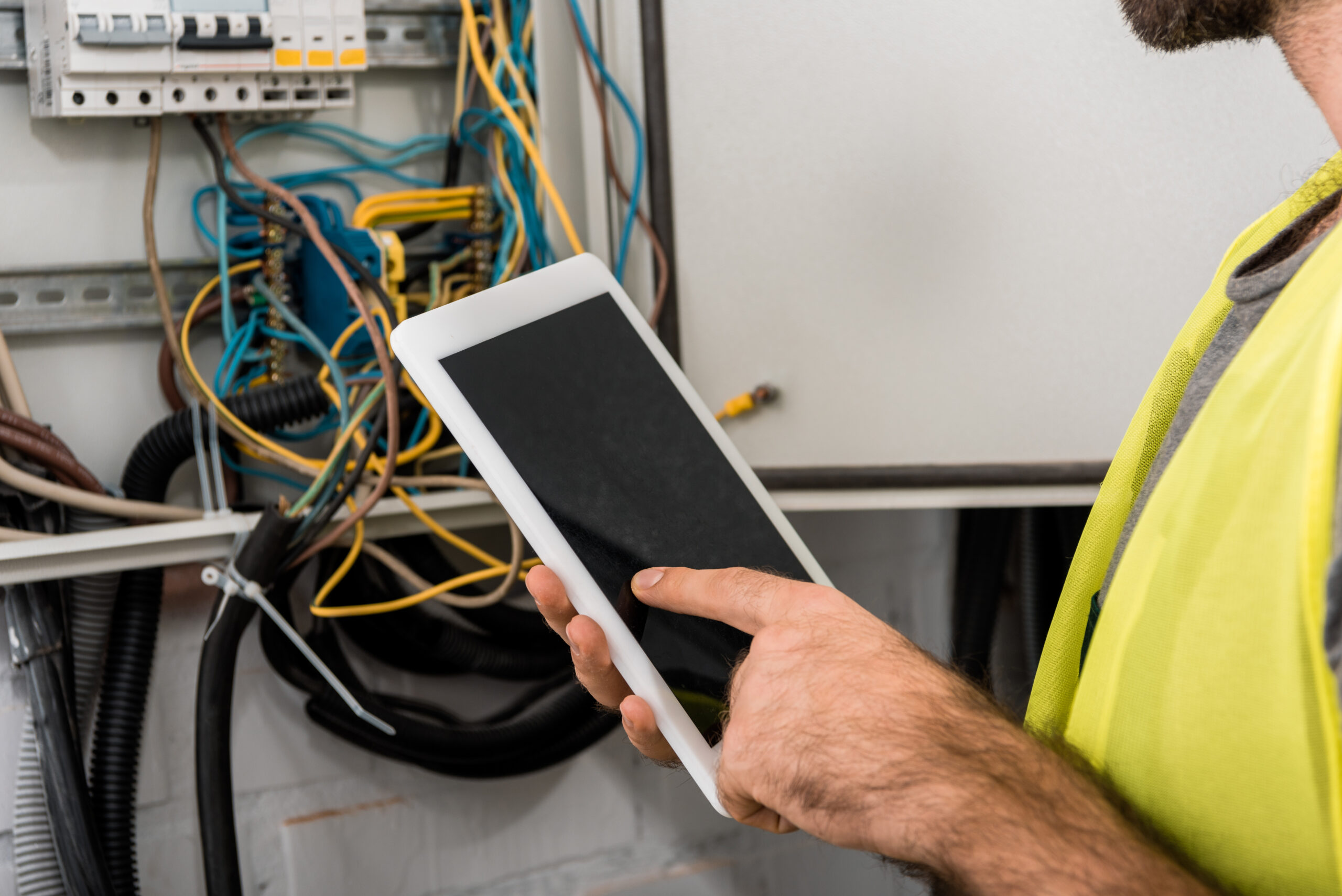 Techniker überprüft einen geöffneten Schaltschrank und dokumentiert Messwerte oder Wartungsdaten auf einem Tablet.
