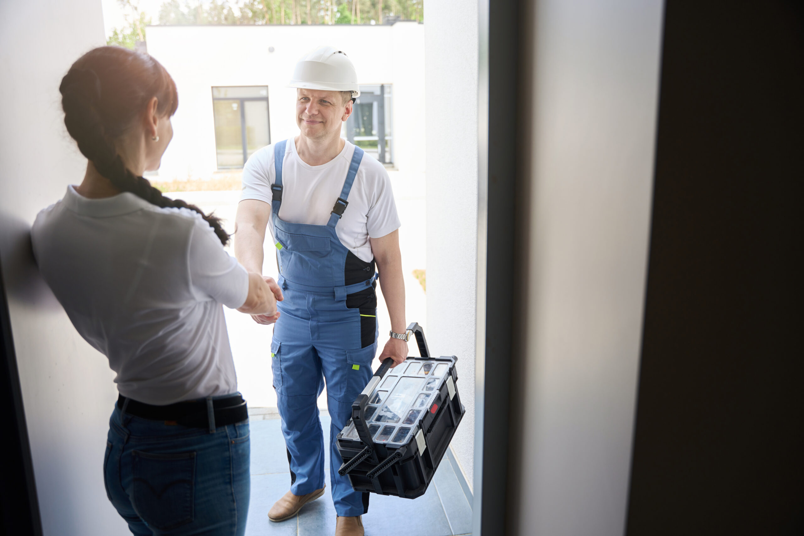 Servicetechniker begrüßt eine Kundin an der Haustür und ist für einen Vor-Ort-Termin mit Werkzeugkoffer angekommen.